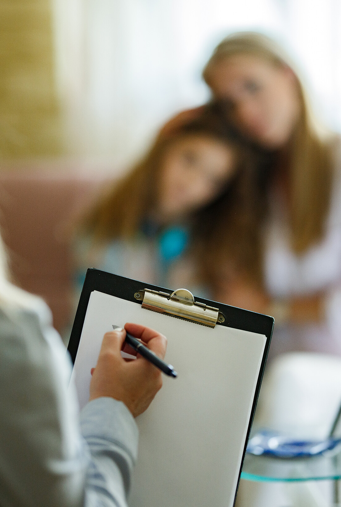 Psychologist taking notes during therapy session whit teenager girl and her mother